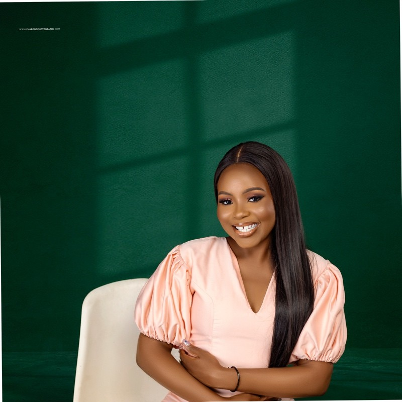 Fatimah Adebowale smiling, wearing a peach blouse against an emerald background